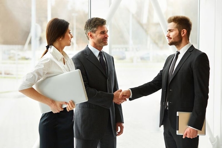 Three people in suits with two people shaking hands