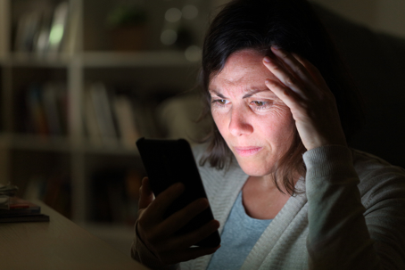 adult woman reading on smart phone lighted screen sitting at night at home