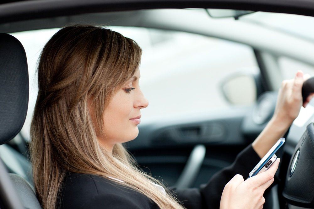 Beautiful businesswoman sending a text while driving to work