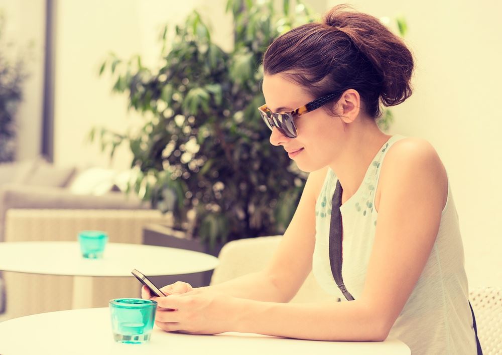 Happy girl texting on the smart phone in a hotel restaurant terrace