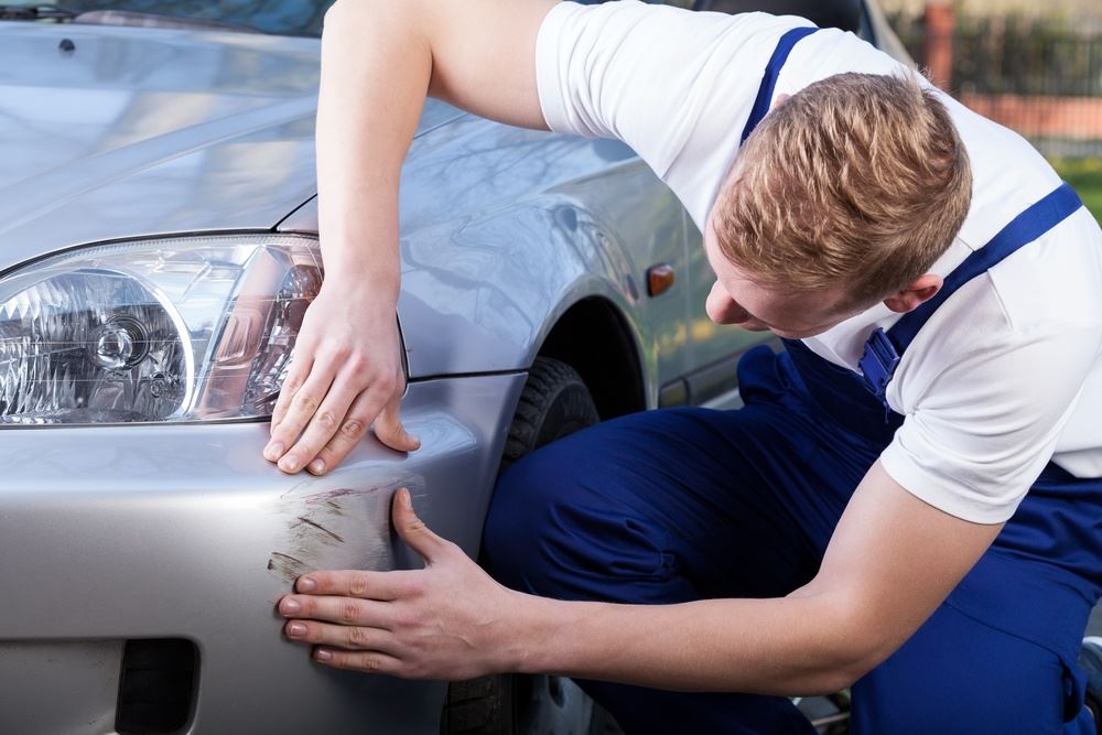 Mechanic In Uniform Assess The Damage On The Car