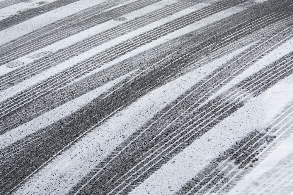Multiple tracks of car tires with a few footprints in snow on pavement
