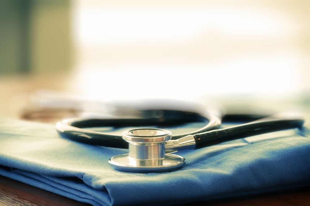 Stethoscope with blue doctor coat on wooden table